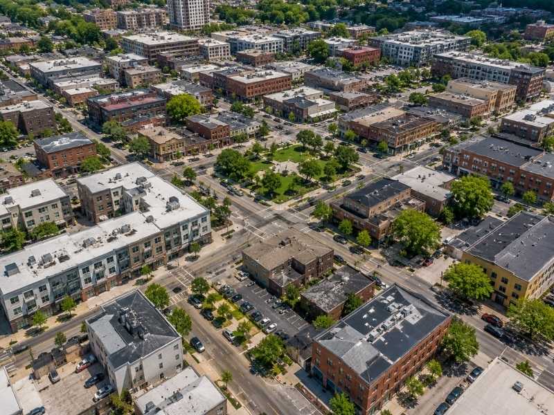 Aerial view of a modern city block with interconnected streets, mixed-use buildings, sidewalks, green spaces, and organized urban infrastructure illustrating contemporary city planning.